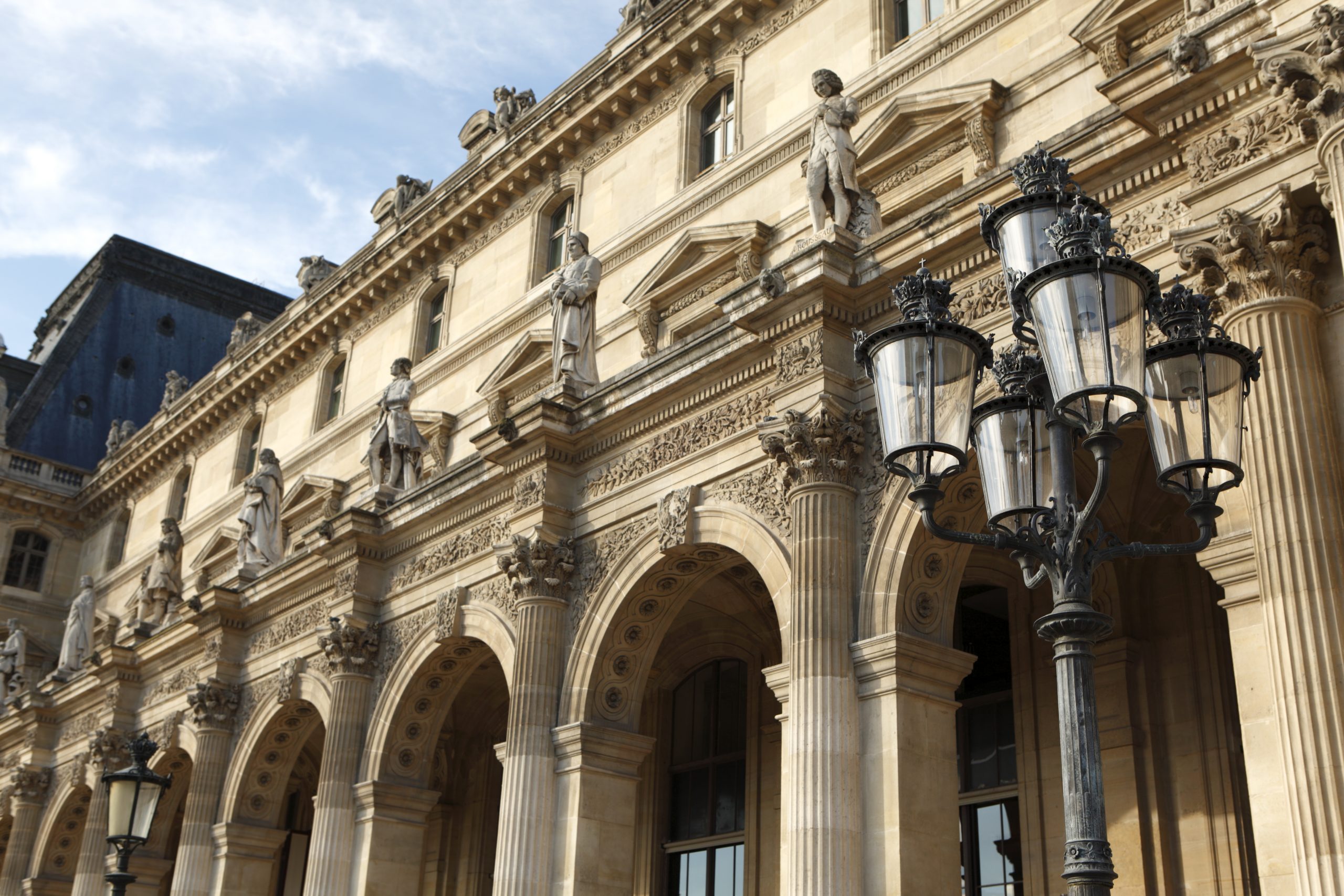 Renaissance architecture and street lamp at the Louvre Museum in Paris bathed in warm late afternoon light.